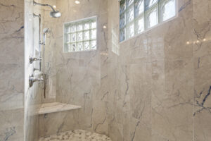 Elegant marble-tiled shower with glass block windows and pebble floor.