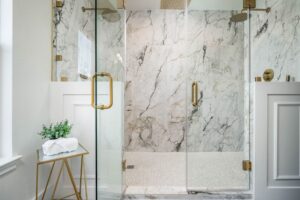 Modern marble bathroom with glass shower and gold fixtures.
