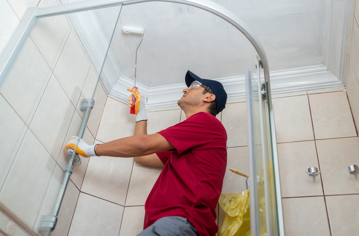 Man painting bathroom ceiling with roller