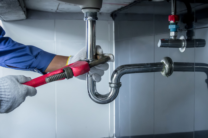 Plumber tightening sink pipe with red wrench